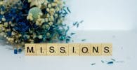 missions, a scrabble type block spelling the word miss, sits next to a bouquet